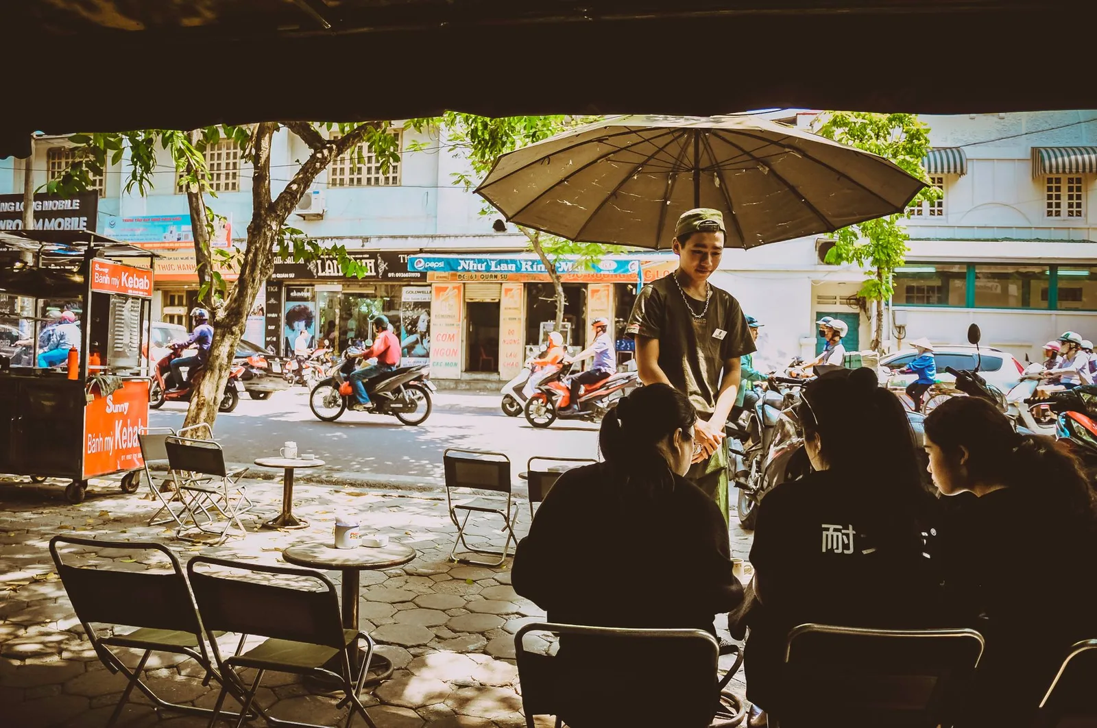 Street food vendor scene in a Hanoi market with locals seated nearby