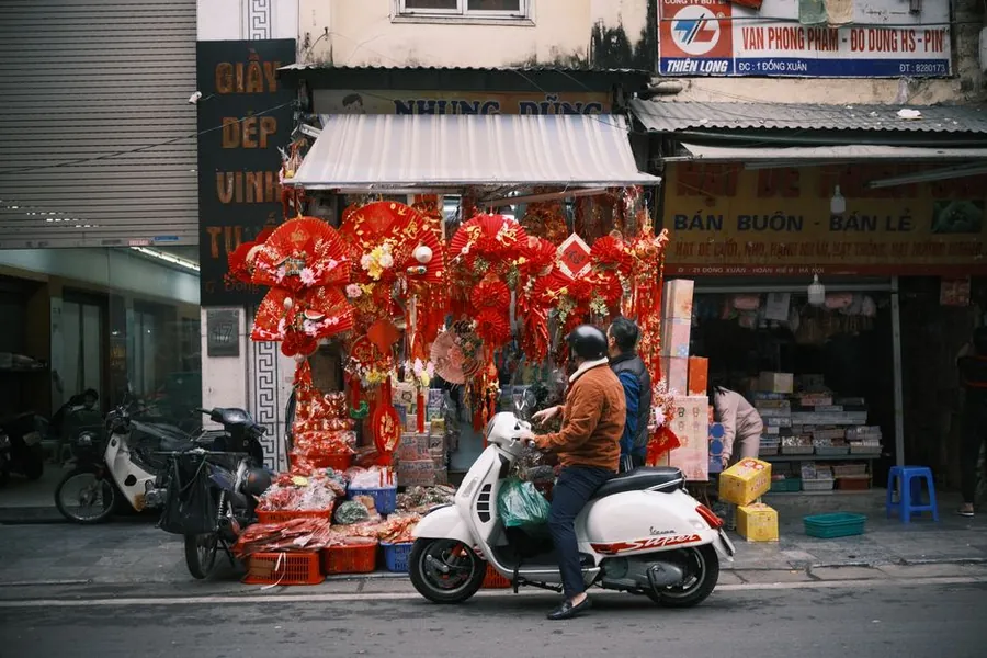 Two people riding a scooter past a lit-up street market in Vietnam